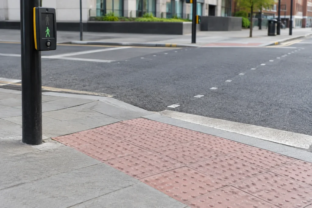 A close view of tactile paving, a dropped kerb and pedestrian crossing signals at an ordinary urban junction