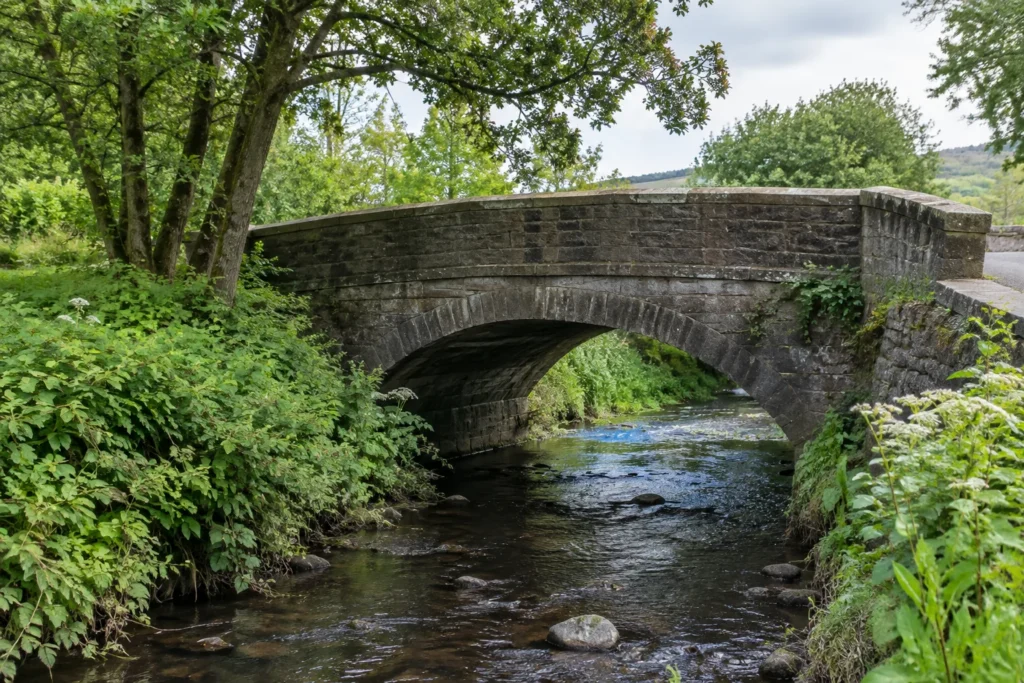 A small masonry bridge over a stream, with stone parapets and leafy banks