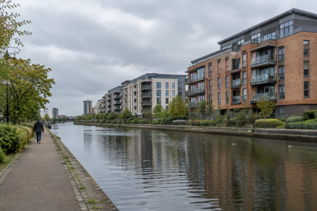 A canal beside modern apartment buildings under an overcast sky, viewed from a public waterside path