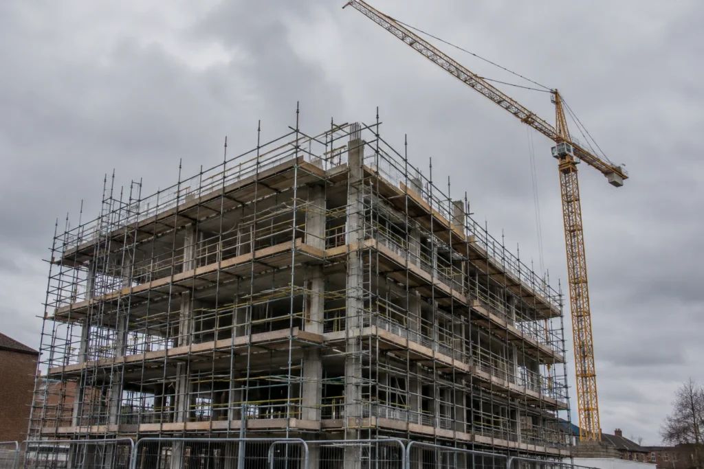 A concrete building frame beneath scaffolding with a crane against an overcast sky