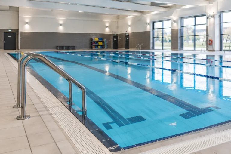 An empty indoor swimming pool with stainless steel handrails and a tiled surround
