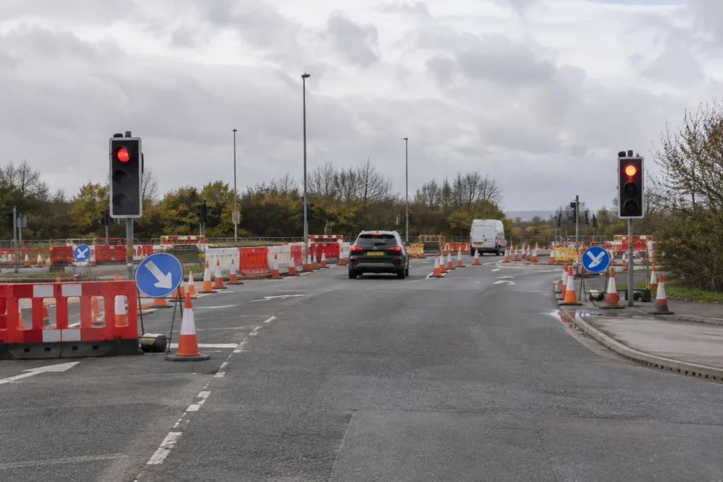 A road junction with temporary traffic lights, cones and barriers in overcast daylight, without readable signs or identifiable landmarks