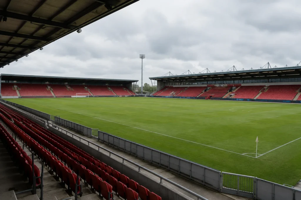 An empty generic football ground with covered seating and a grass pitch beneath an overcast sky