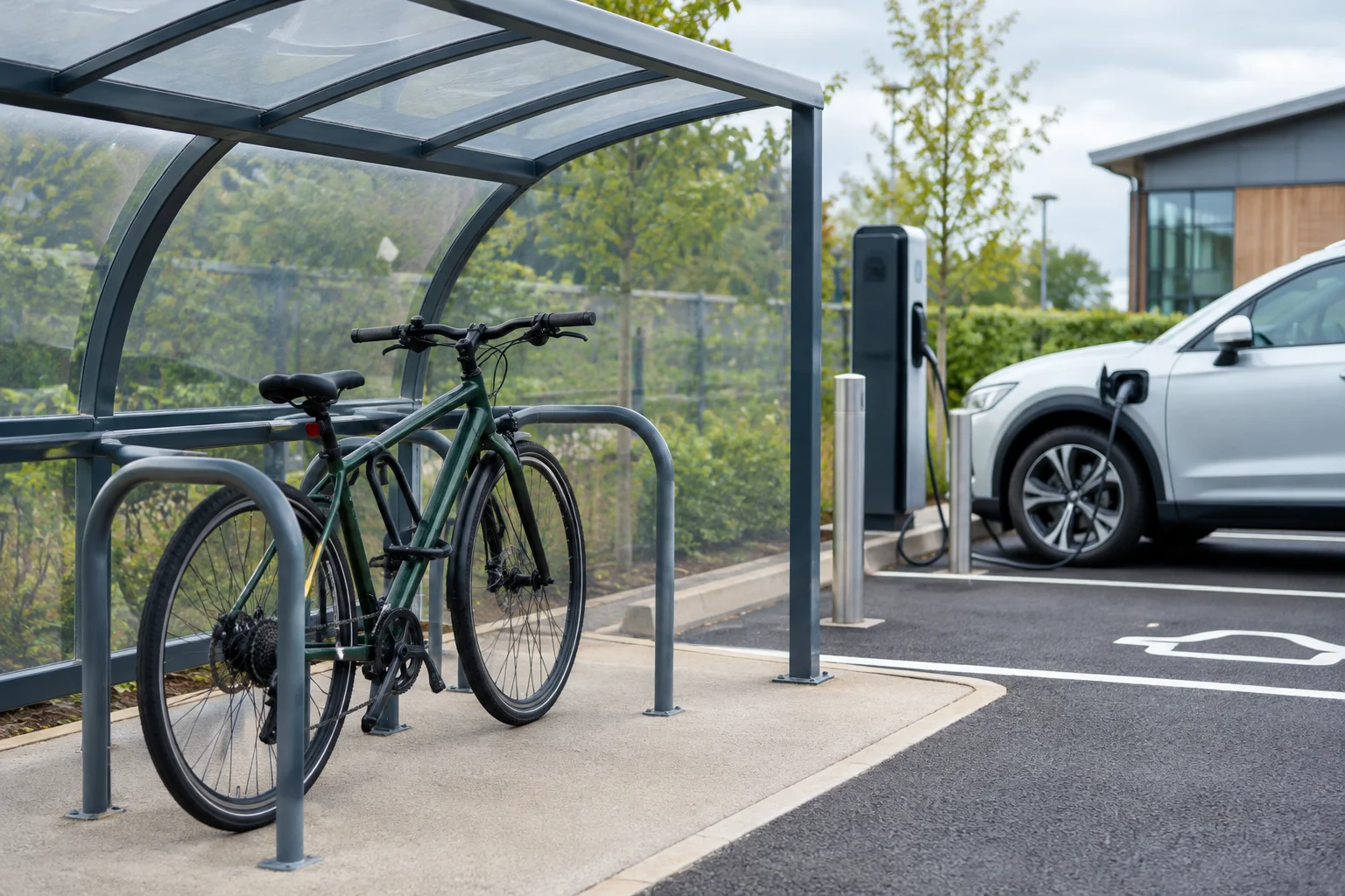 A bicycle secured in a covered cycle rack beside an electric car charging bay, with no readable signs