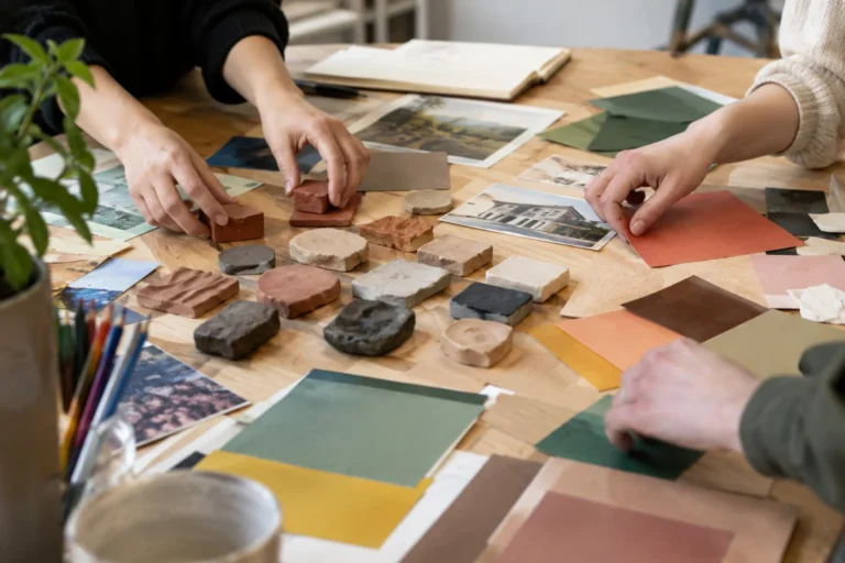 Anonymous hands arranging clay samples and coloured paper around a communal workshop table